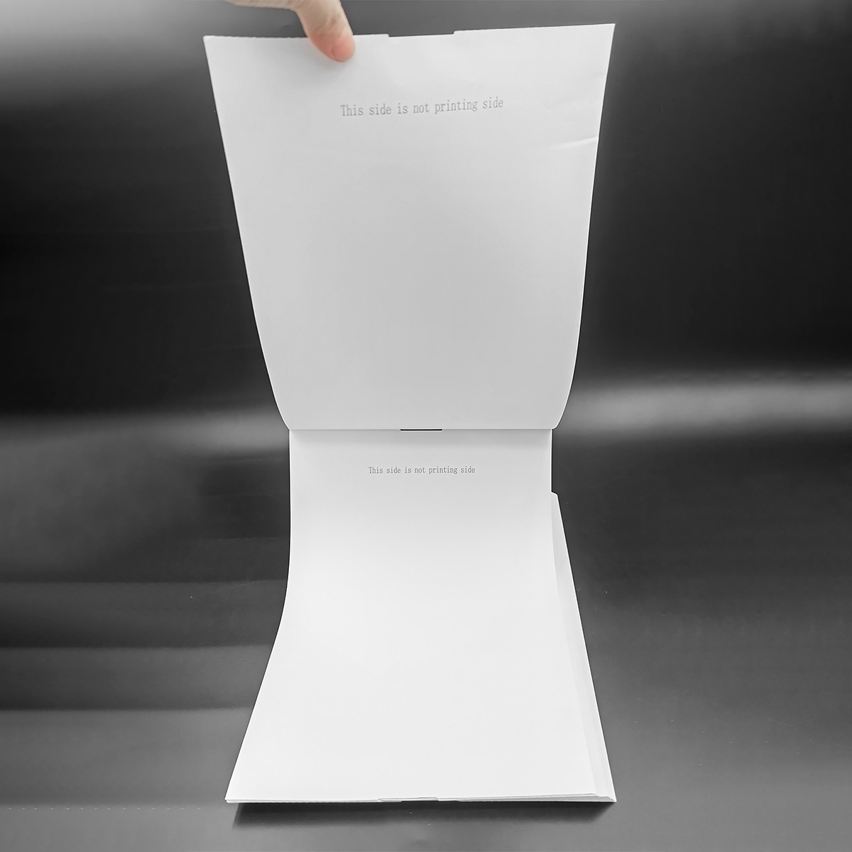 Dłoń trzyma otwarta księgę pustego białego papieru na ciemnym tle.