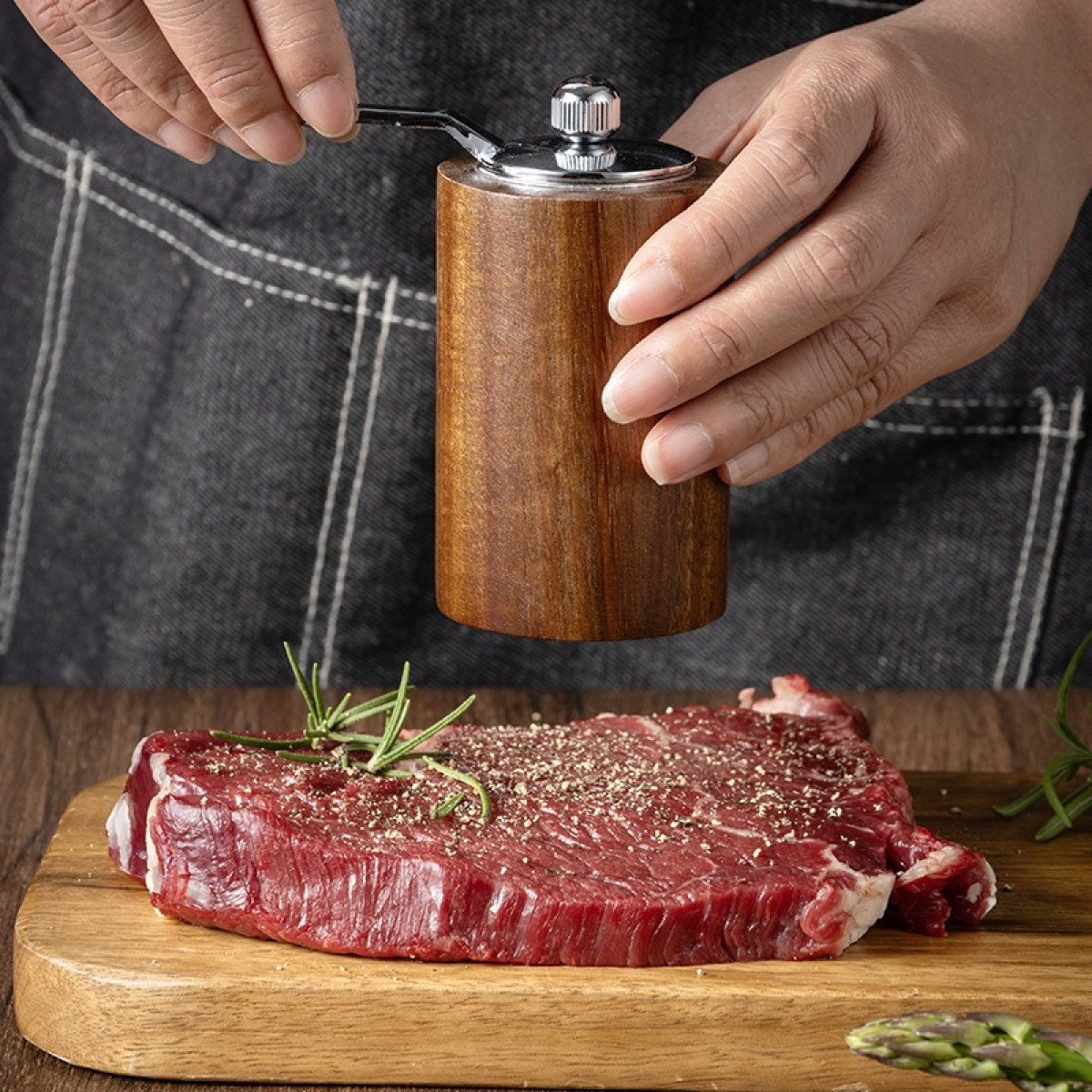 Drewniany młynek mieli przyprawy nad surowym stekiem na desce.