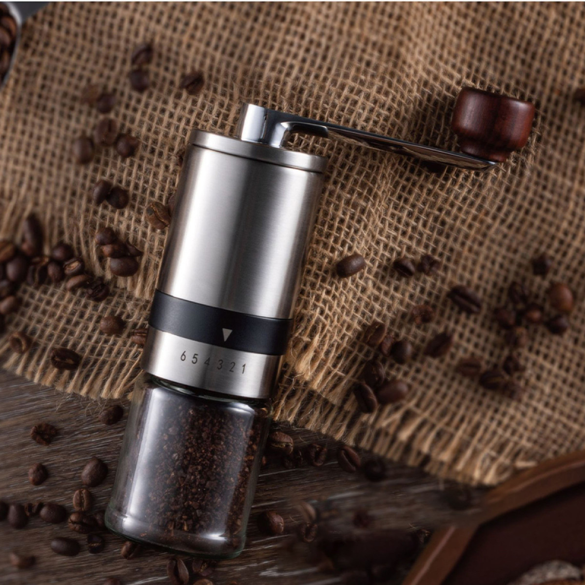 Srebrny ręczny młynek do kawy z drewnianą rączką na płótnie z ziarnami.