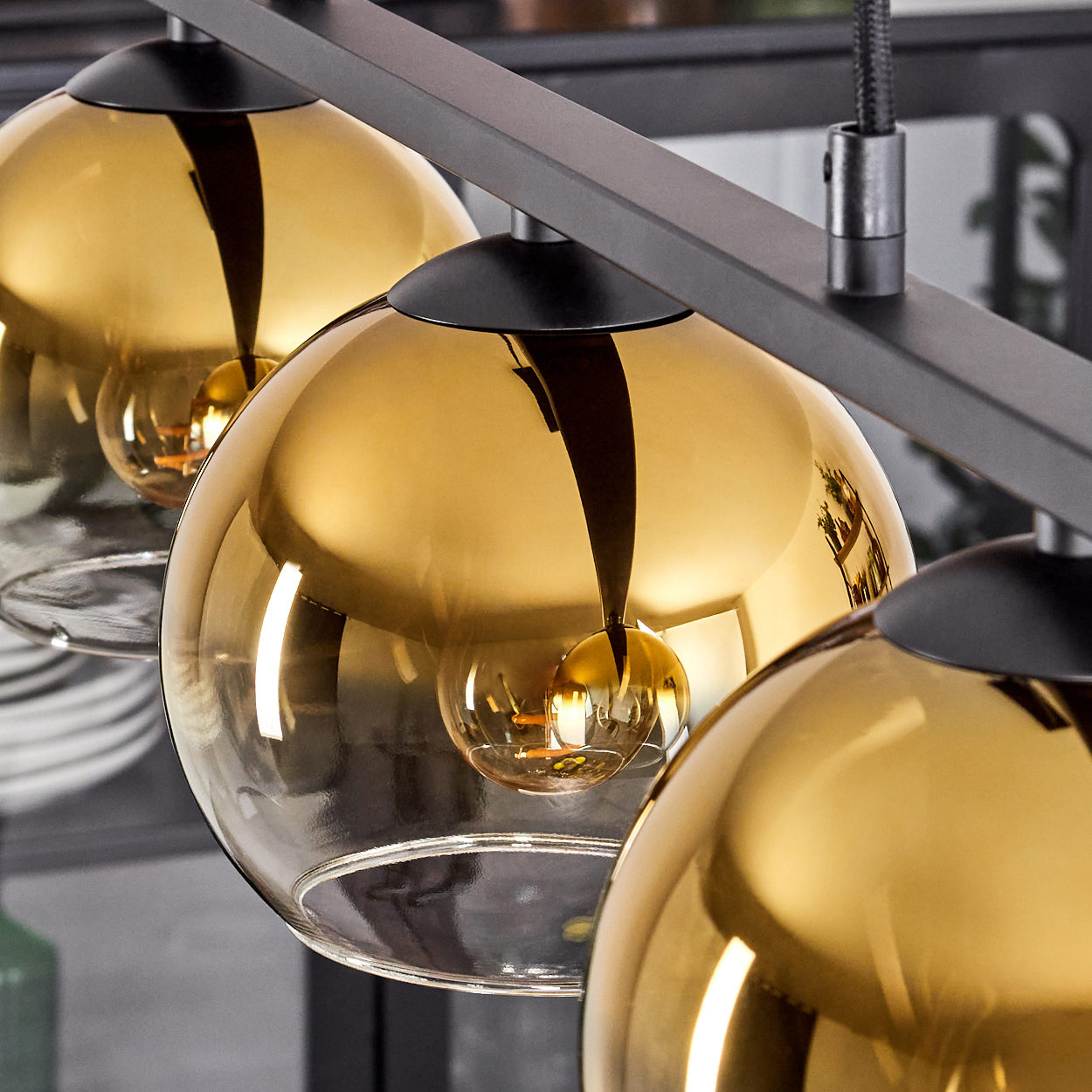 Dreiflammige Pendelleuchte mit goldenen Glaskugeln und schwarzem Gestell.