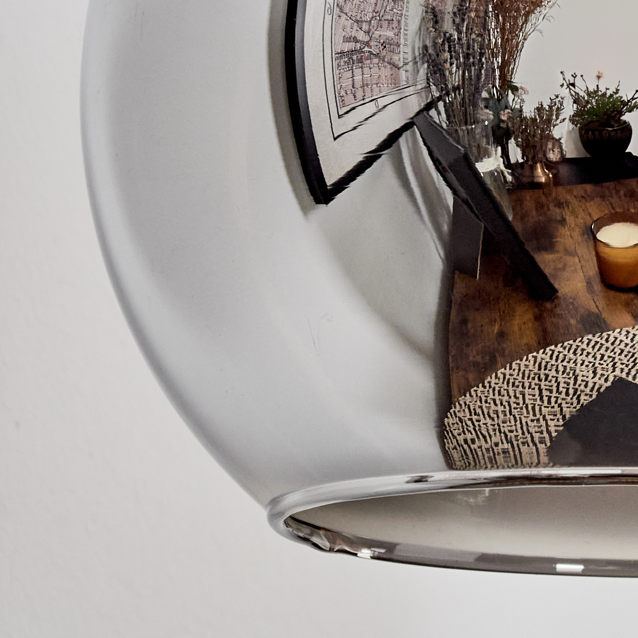 Ein Spiegel reflektiert eine Karte, Trockenblumen, eine Kerze und eine Pflanze auf einem Holztisch.
