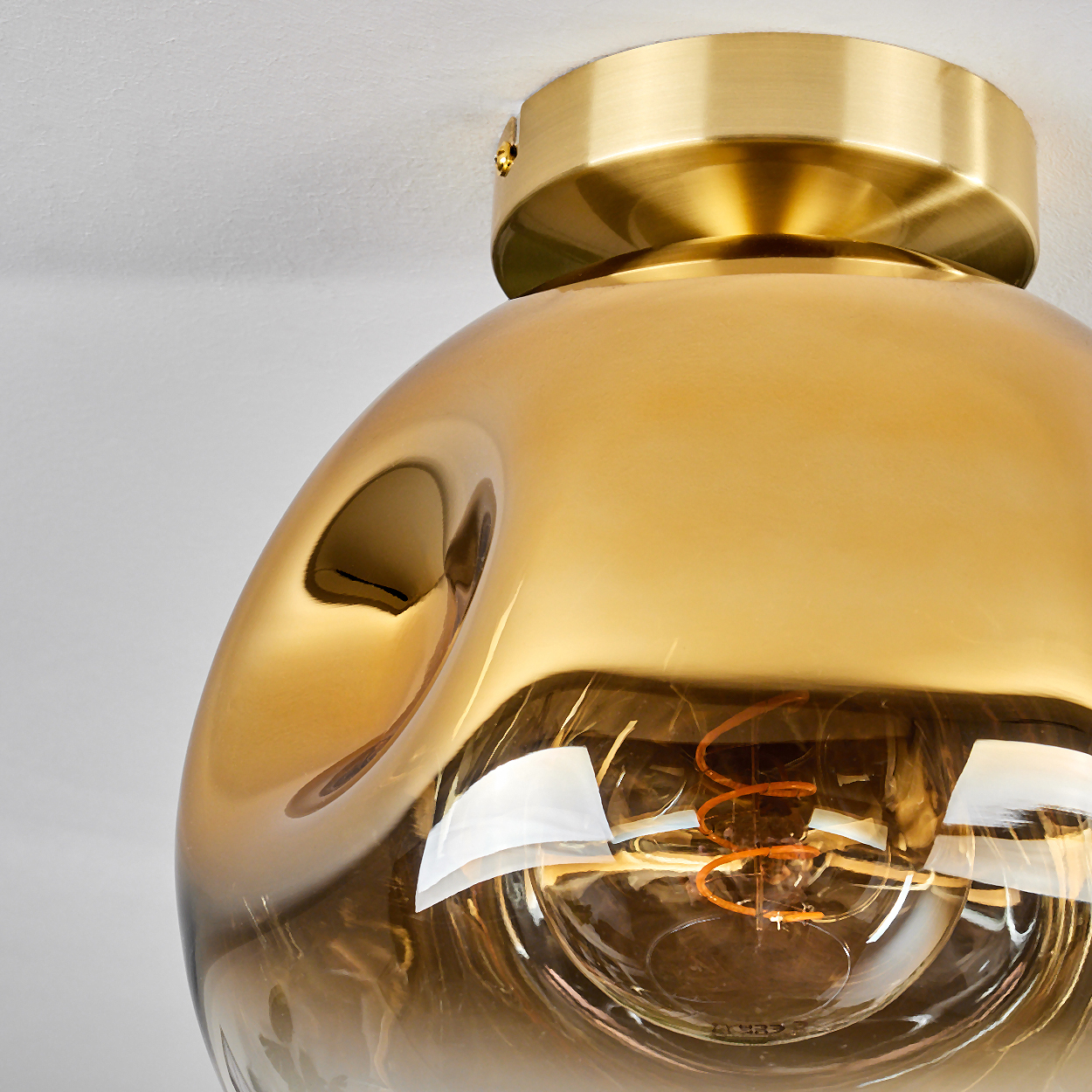 Eine goldene Lampe mit bernsteinfarbenem Glas und sichtbarem Glühfaden.