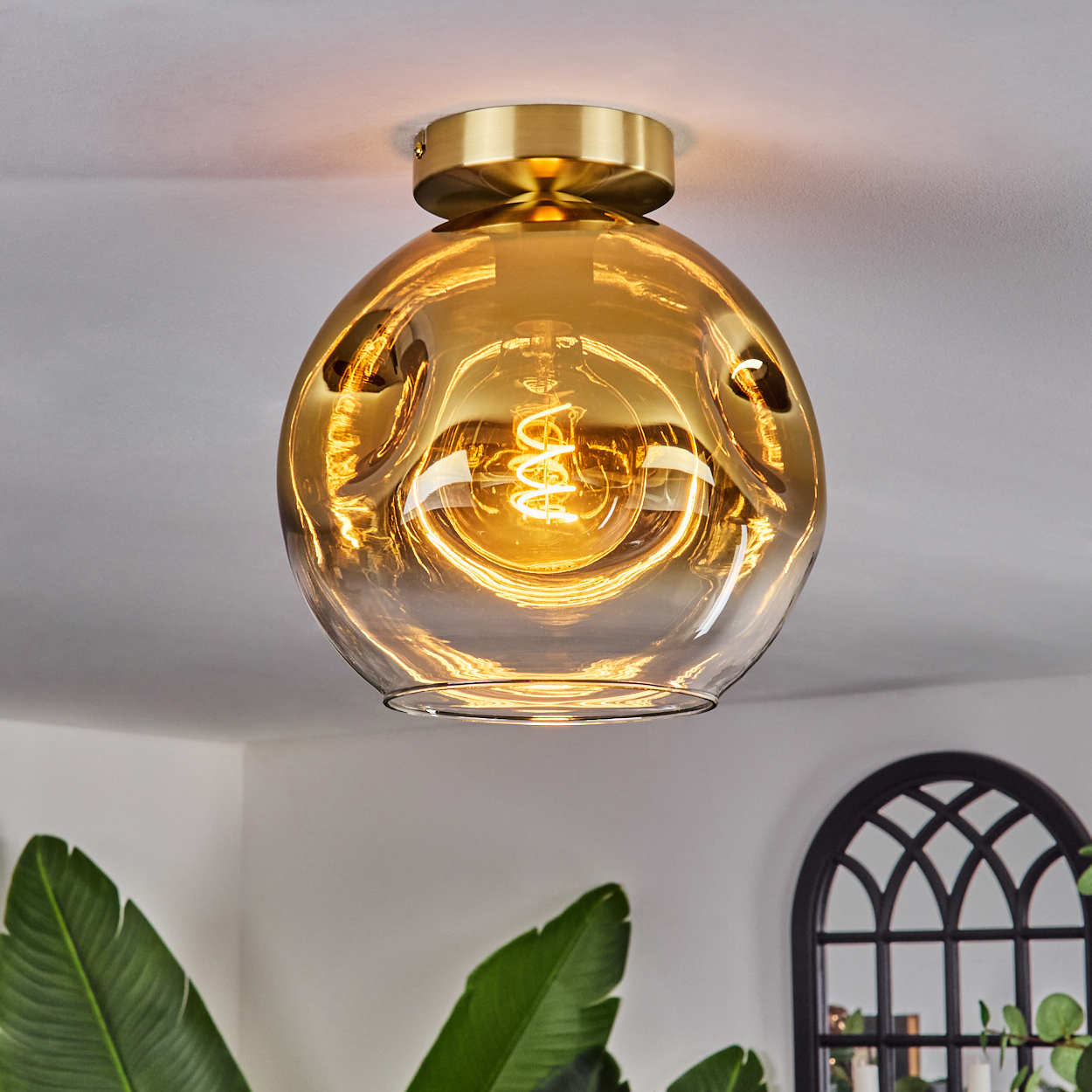 Eine goldene Glaskugel-Deckenleuchte mit sichtbarer Glühbirne.