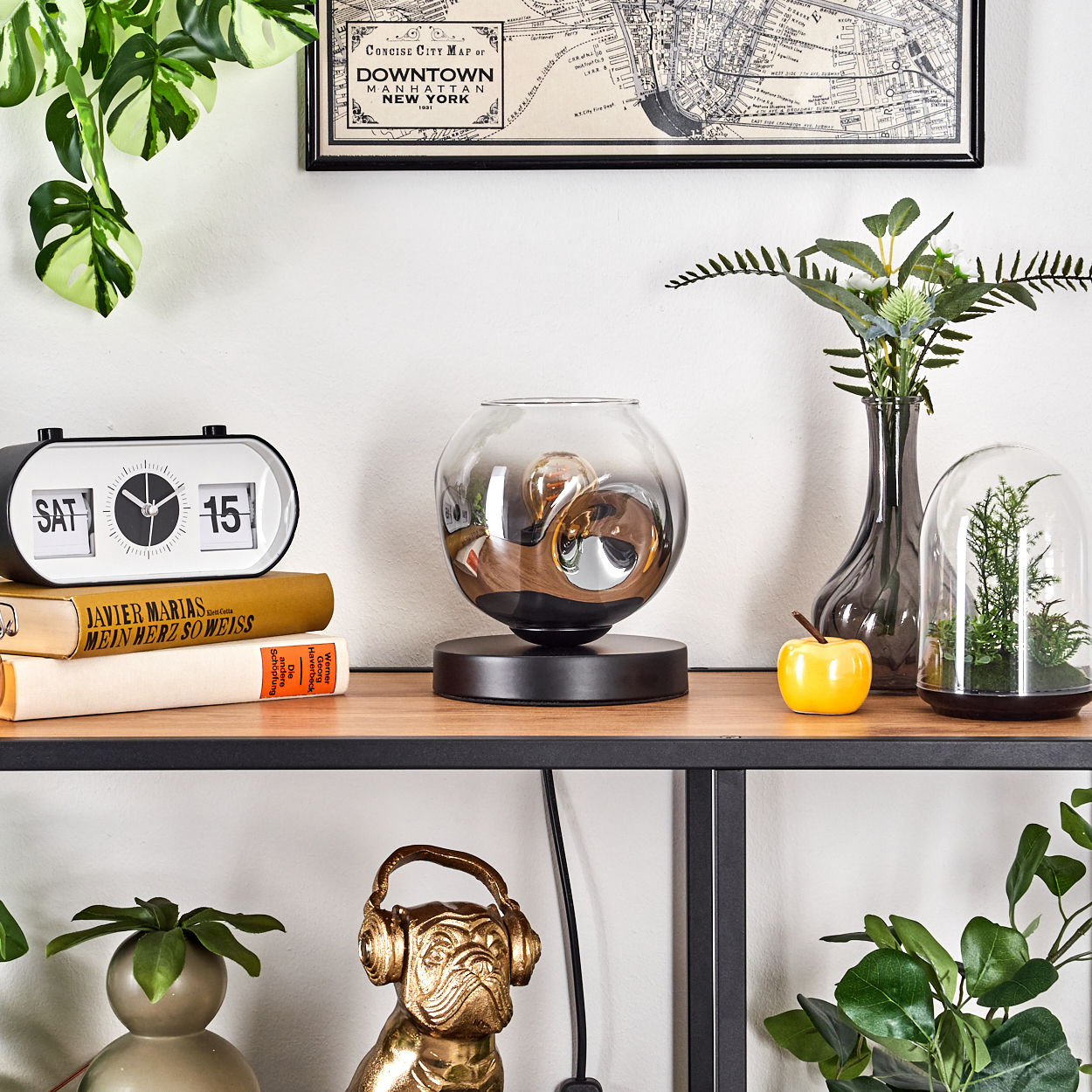 Ein Bücherregal mit Dekorationsgegenständen wie einer Lampe, einem Wecker, Büchern und Pflanzen.