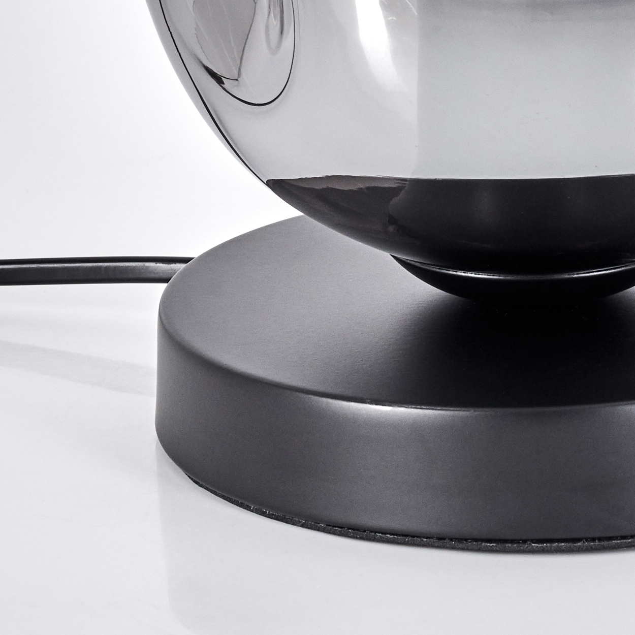 Schwarzer Sockel einer Lampe mit spiegelnder, kugelförmiger Oberseite.