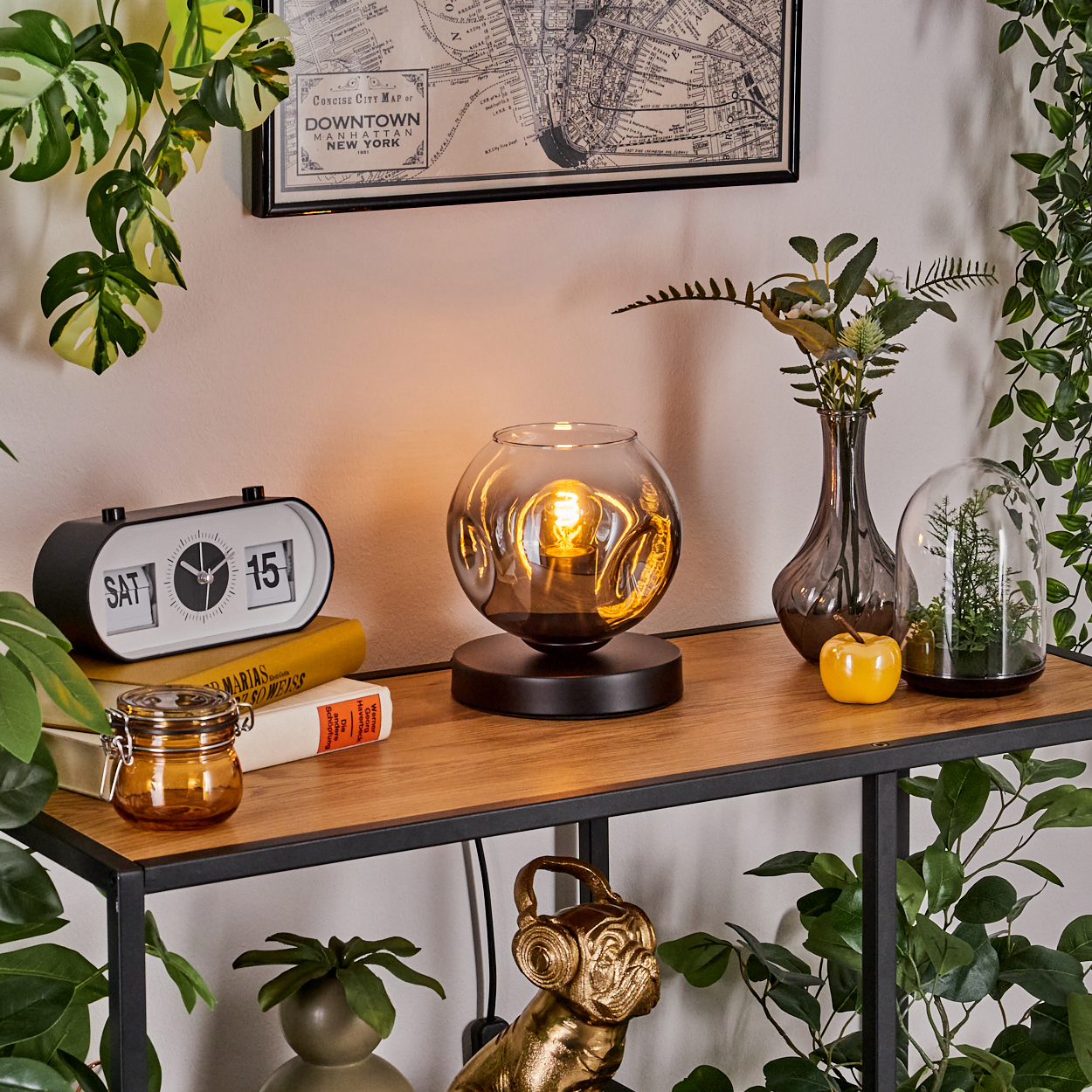 Ein Tisch mit Deko: Lampe, Uhr, Vase, Bücher, Apfel, Pflanze.