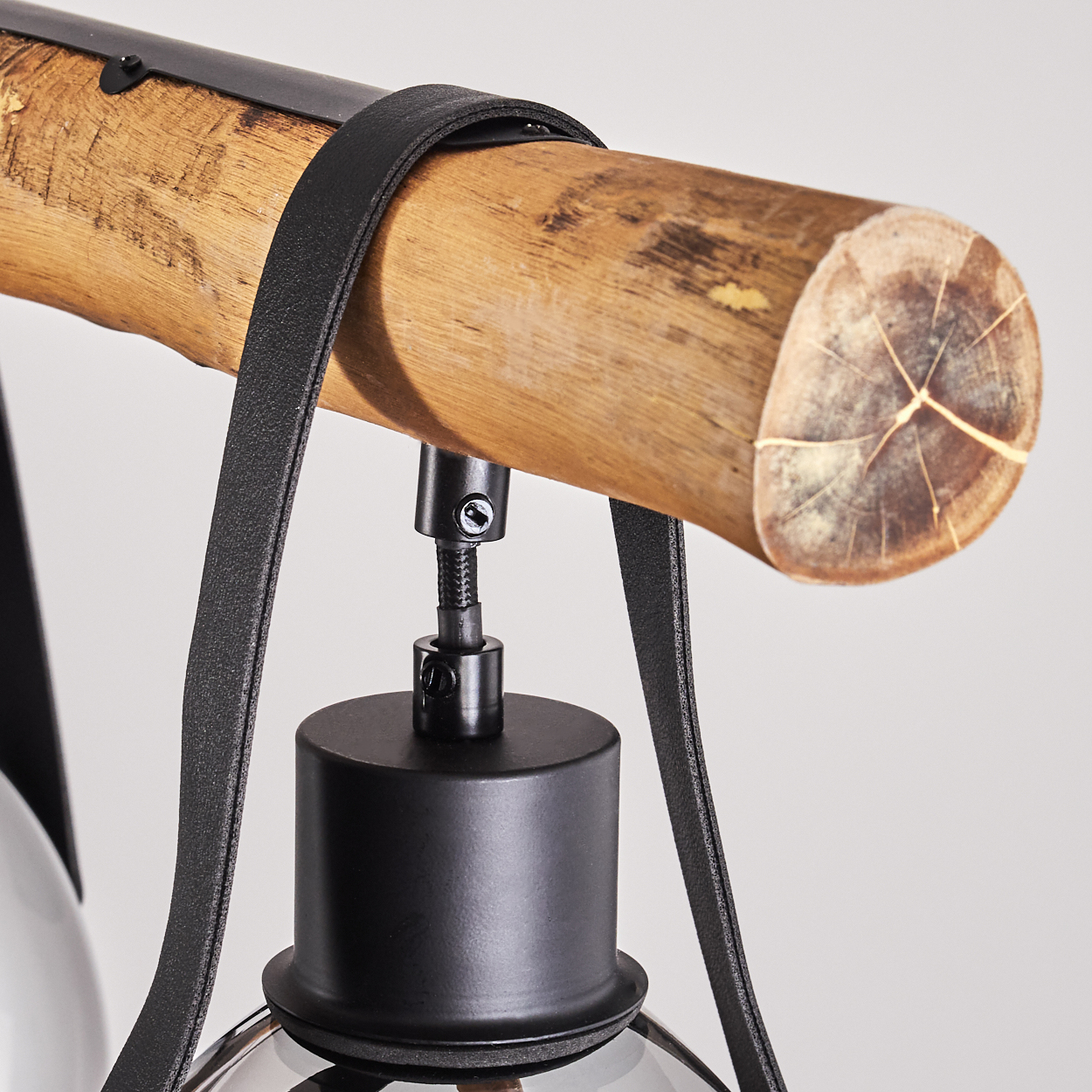Ein hölzerner Ast mit schwarzem Lederband und schwarzer Metallaufhängung für eine Lampe.