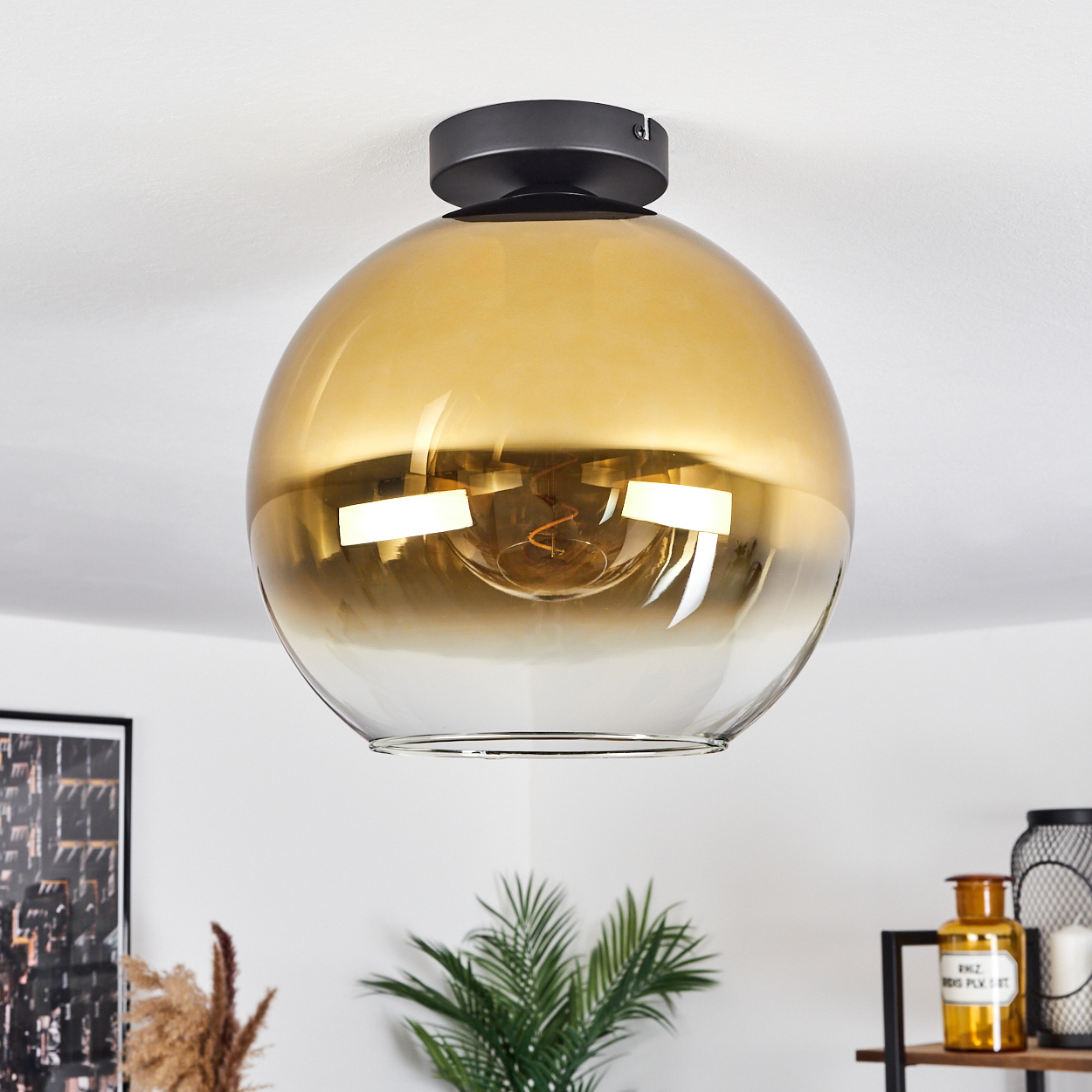 Eine goldene, kugelförmige Deckenleuchte mit schwarzem Sockel hängt an der Decke.