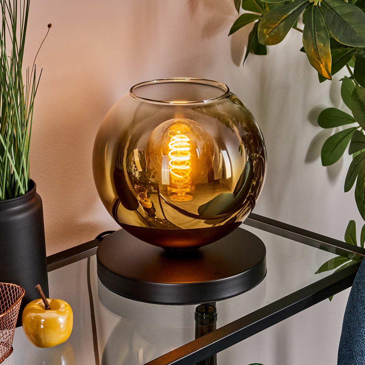 Eine runde bernsteinfarbene Glas-Tischlampe mit sichtbarer Edison-Glühbirne auf einem Glasregal.