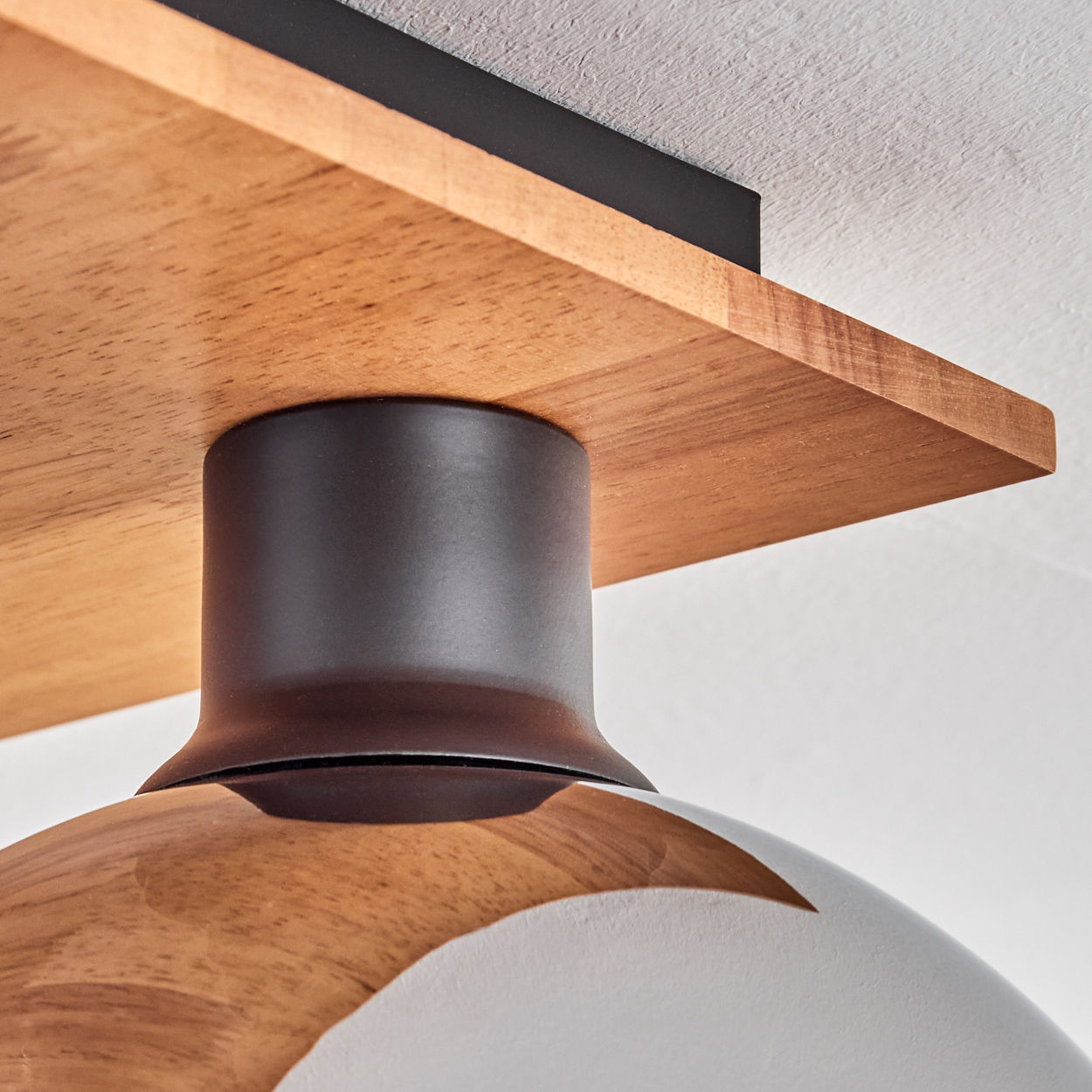 Holzdecke mit dunklem Metallzylinder und weißem Lampenschirm.