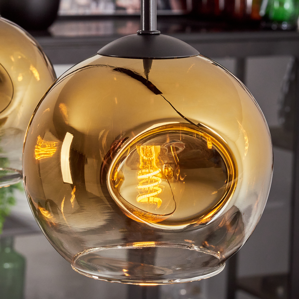 Eine bernsteinfarbene Glaskugel mit Glühfadenlampe hängt von einer schwarzen Halterung.