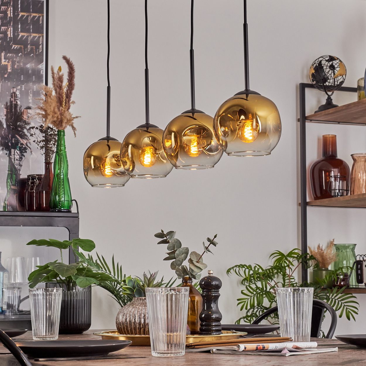 Eine Esszimmer-Hängeleuchte mit bernsteinfarbenen Glaskugeln über einem Holztisch mit Gläsern.
