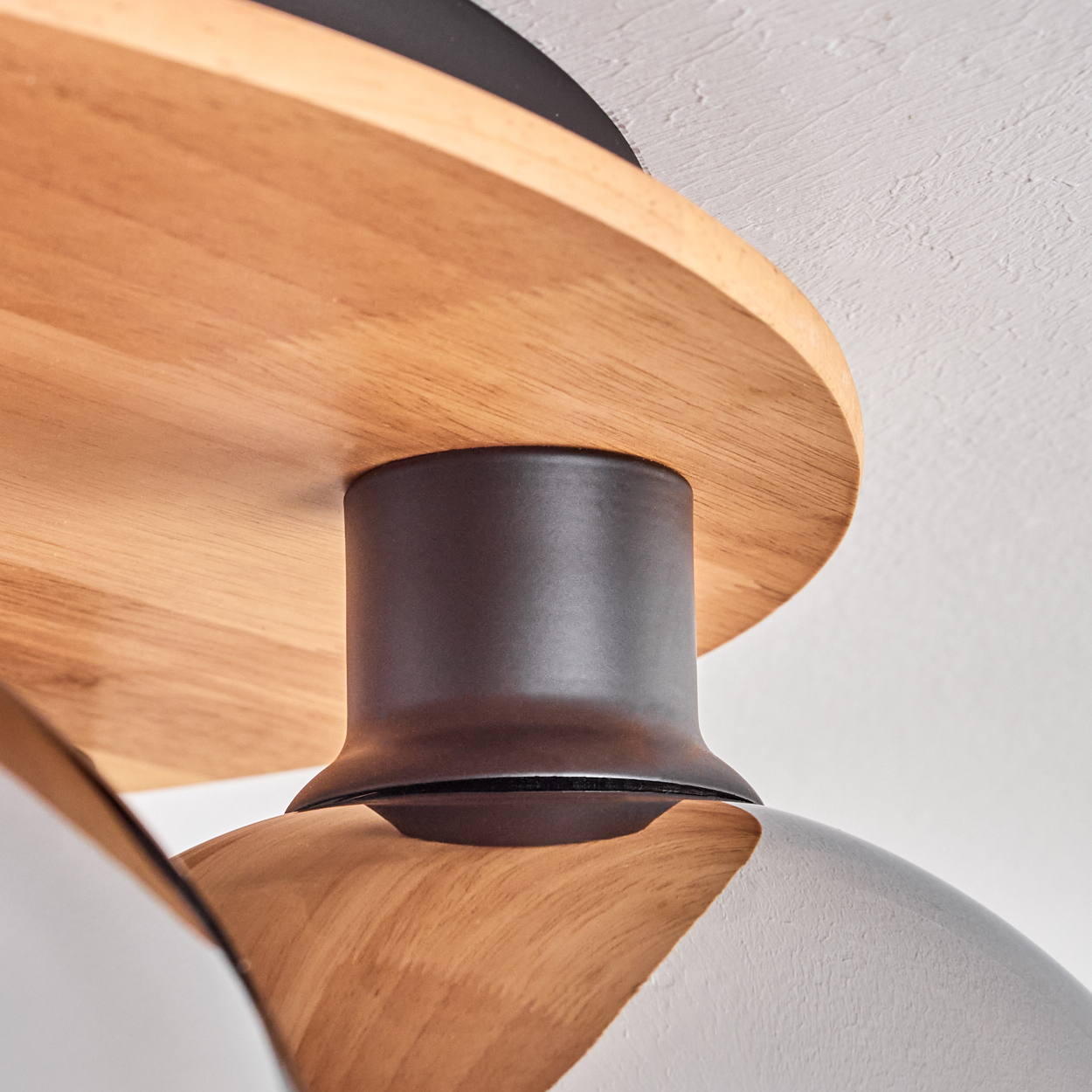 Nahaufnahme einer modernen Lampe mit Holz- und dunklen Metalldetails an einer weißen Decke.