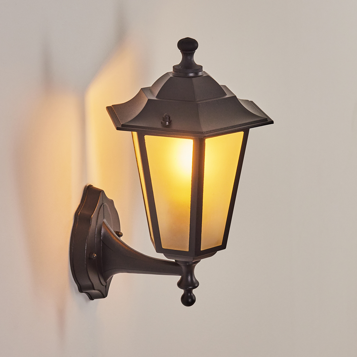 Eine dunkle Wandlaterne mit einem bernsteinfarbenen Licht strahlt an einer Wand.