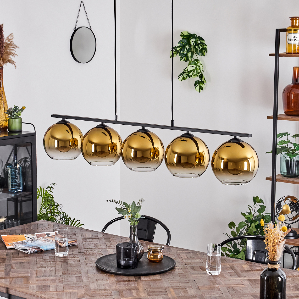 Eine Hängeleuchte mit fünf goldenen Kugelschirmen über einem Holztisch.