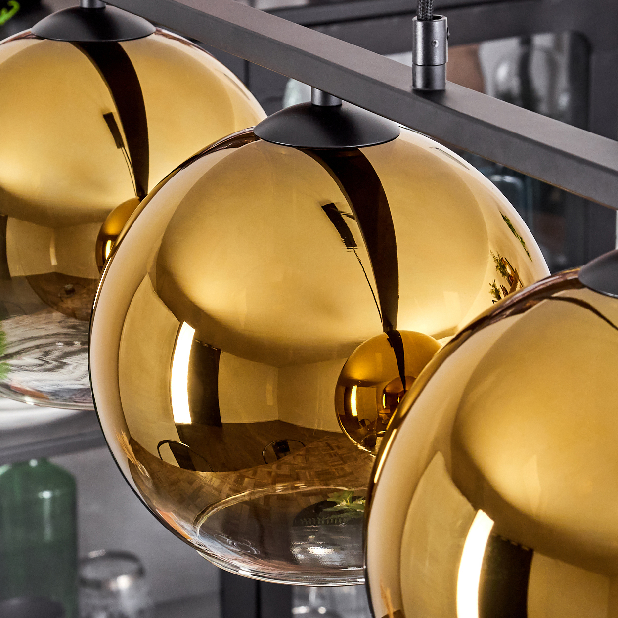 Drei goldene Glaskugeln hängen an einer schwarzen Leiste. Hintergrund unscharf.