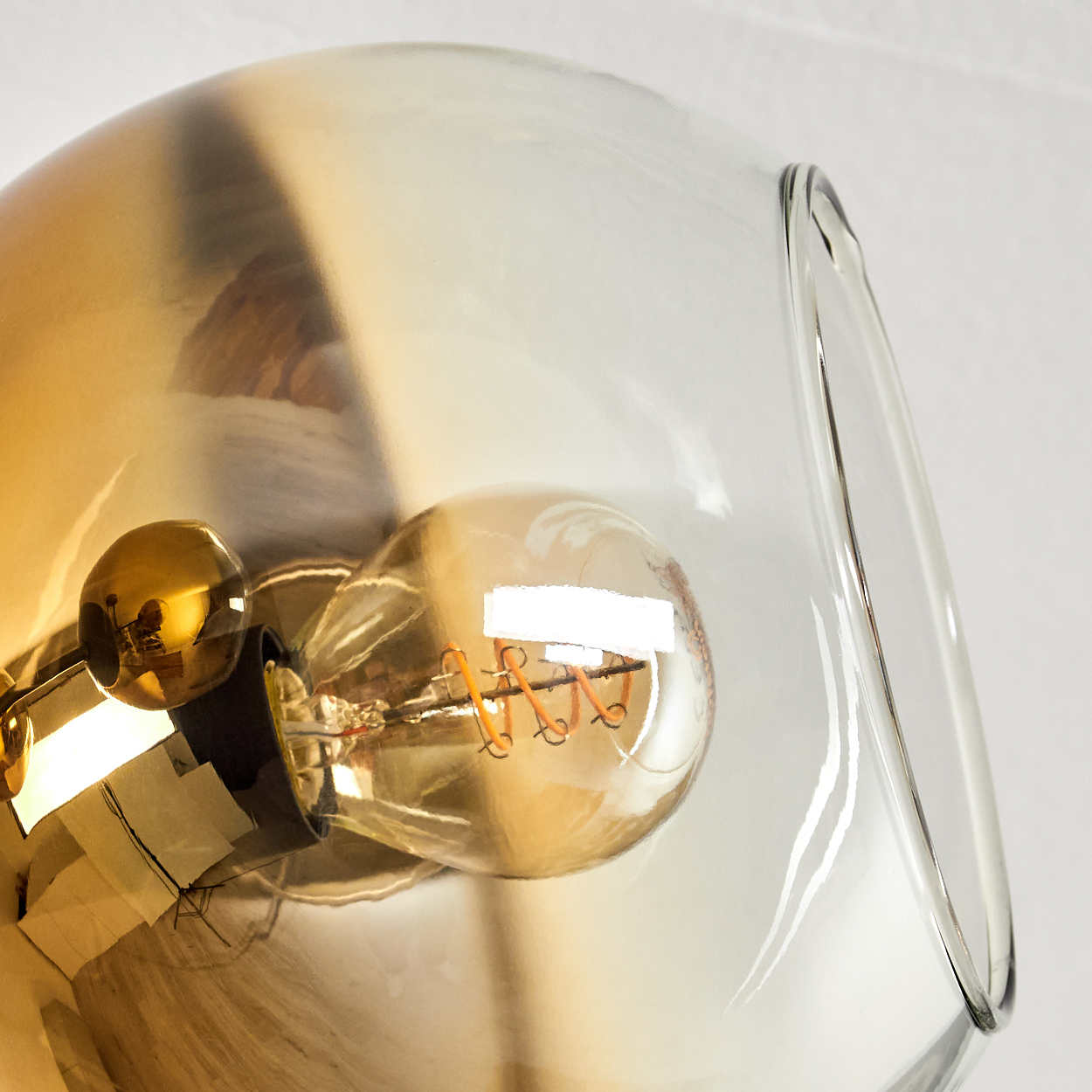 Eine Glühbirne mit Spiralwendel in einer klaren Glasglocke mit goldbraunem Schimmer.