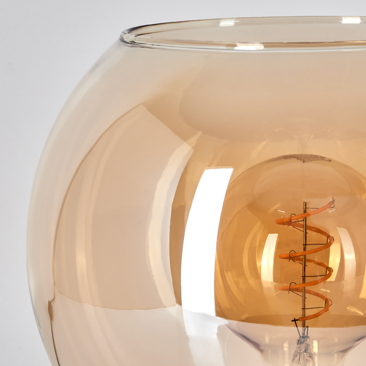 Eine bernsteinfarbene Glühbirne mit Spiralwendel in einem durchsichtigen Glasbehälter.