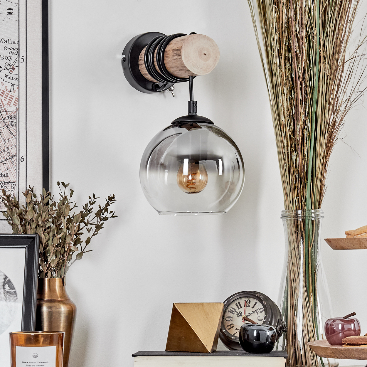 Wandleuchte mit Glasglobus, Holz und Metallakzenten neben Trockengräsern.