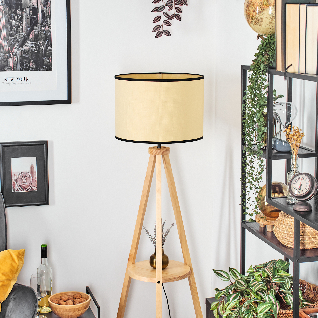 Ein beiger Lampenschirm auf einem Holzständer mit einem Regal, daneben ein Regal mit Büchern und Pflanzen.
