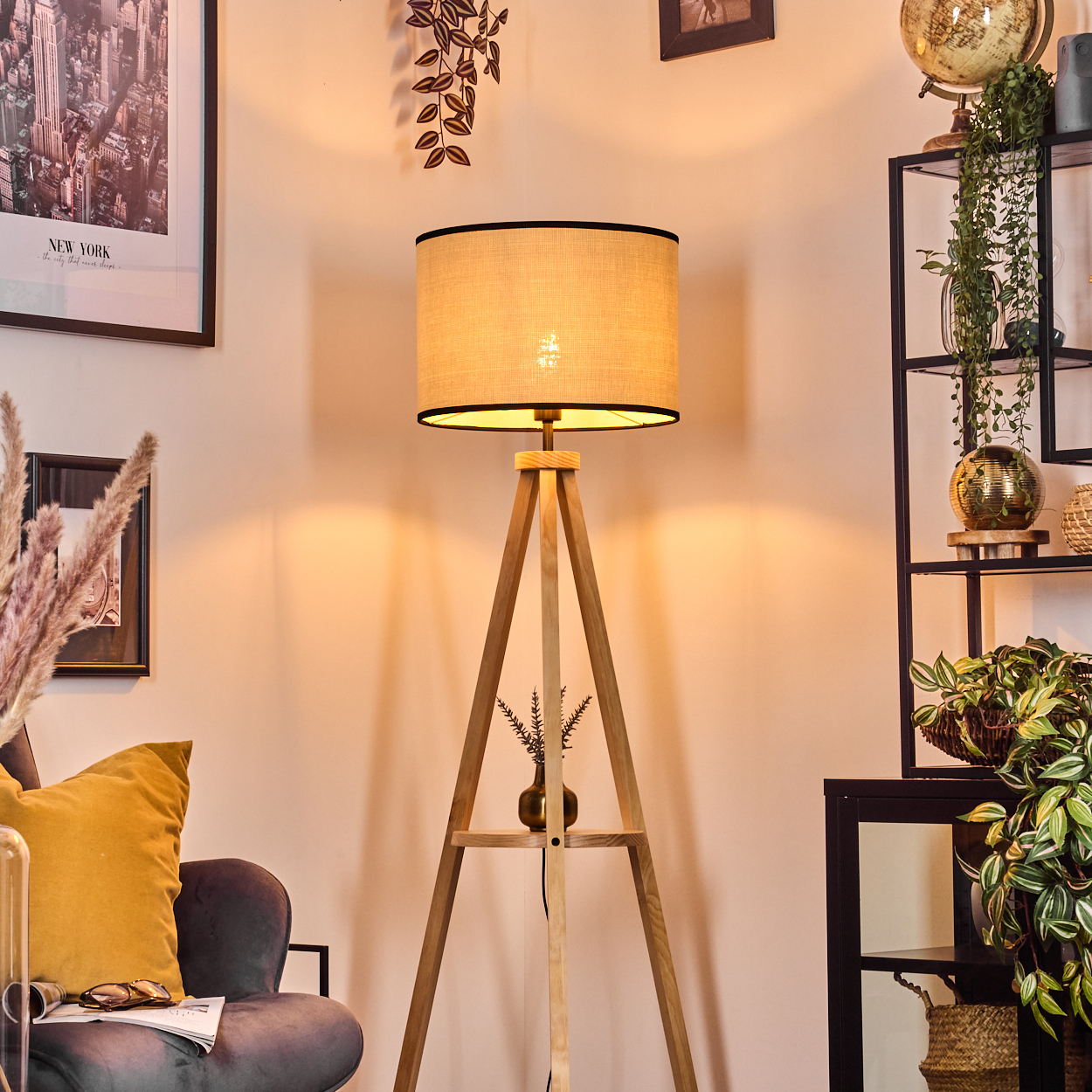 Ein hölzerner Dreibein-Stehlampe mit beigem Lampenschirm steht neben einem Sessel.