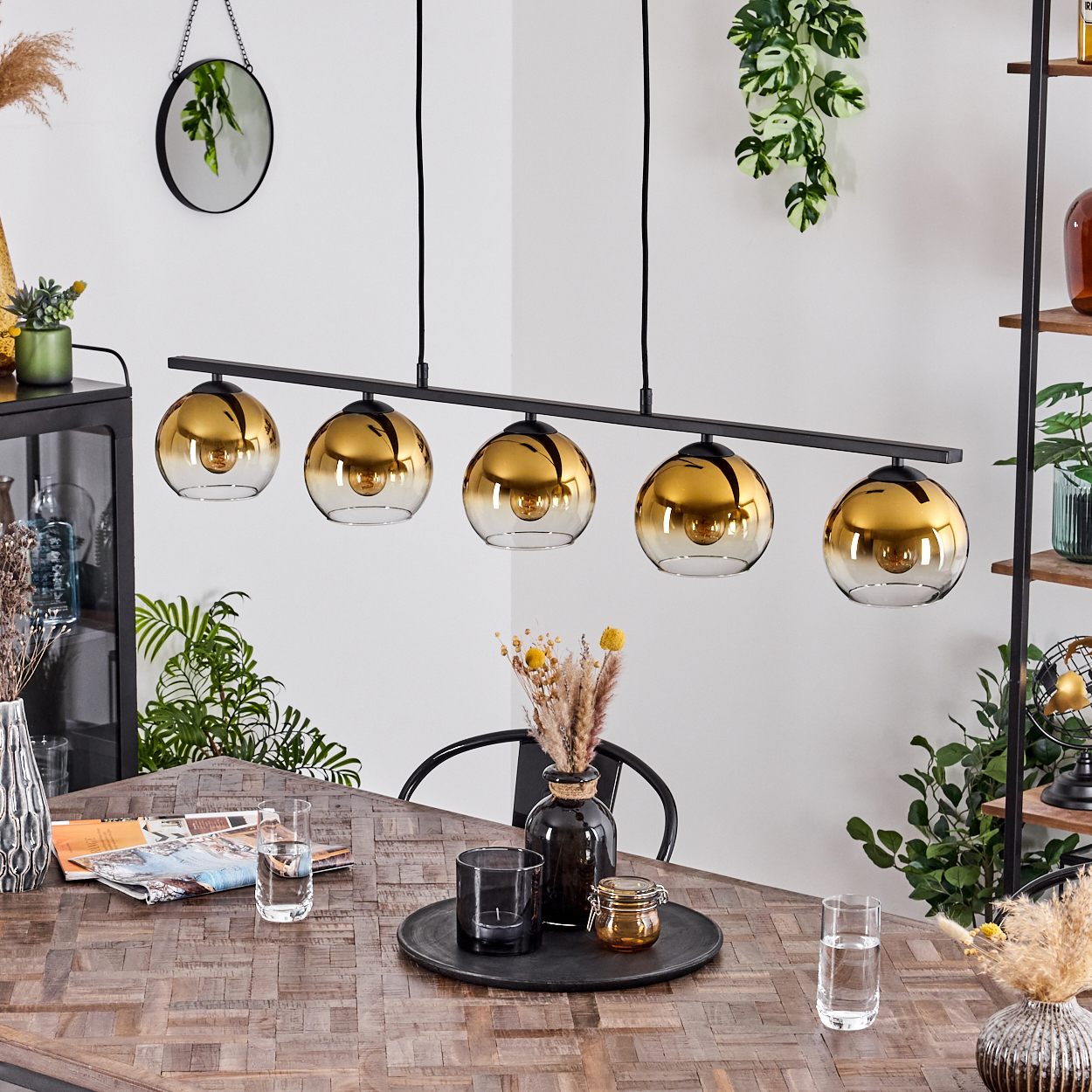 Ein f ünfköpfiger Pendelleuchter mit goldenen Glaskugeln hängt über einem Holztisch.