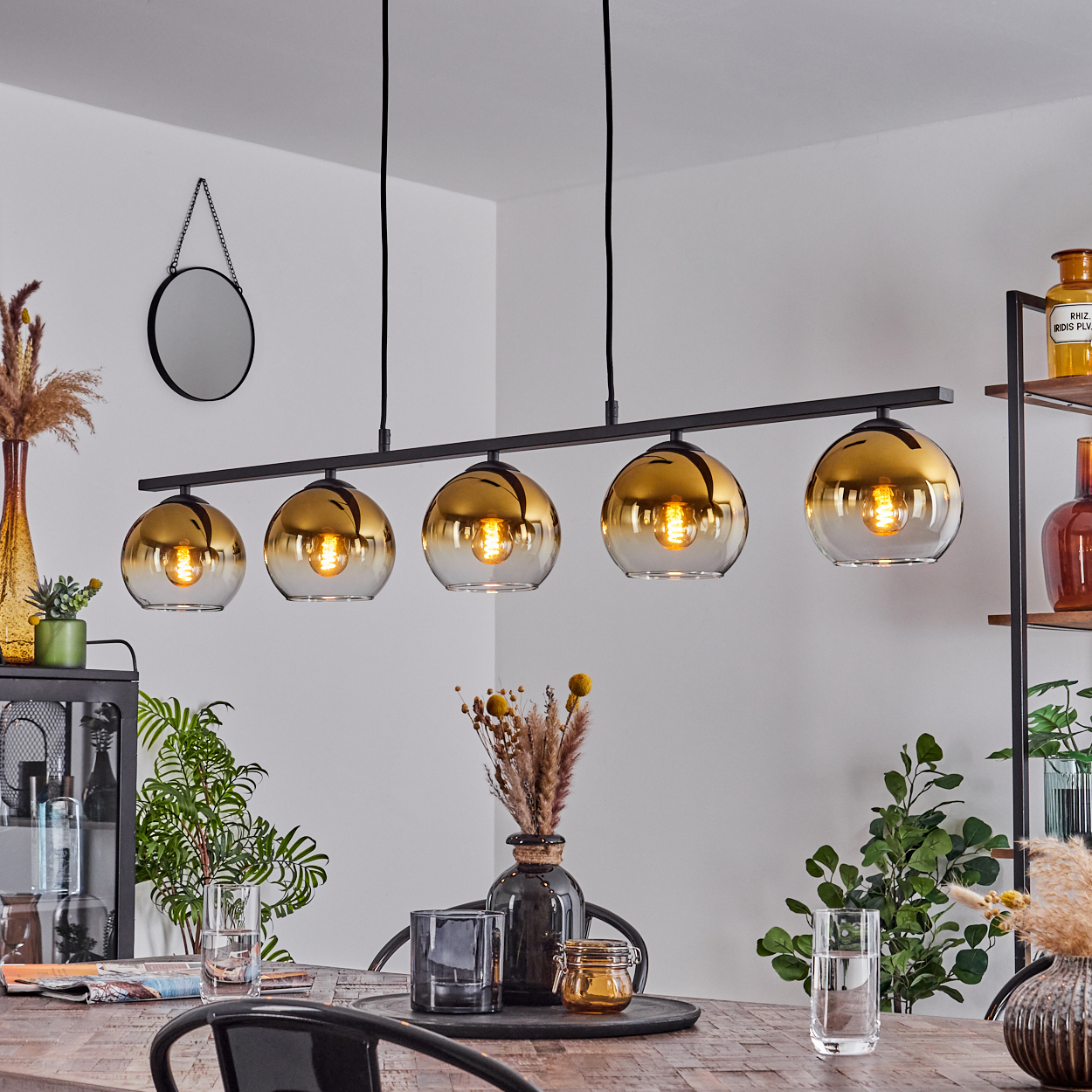 Fünf goldene Glaskugeln hängen an einem schwarzen Balken über einem Holztisch.