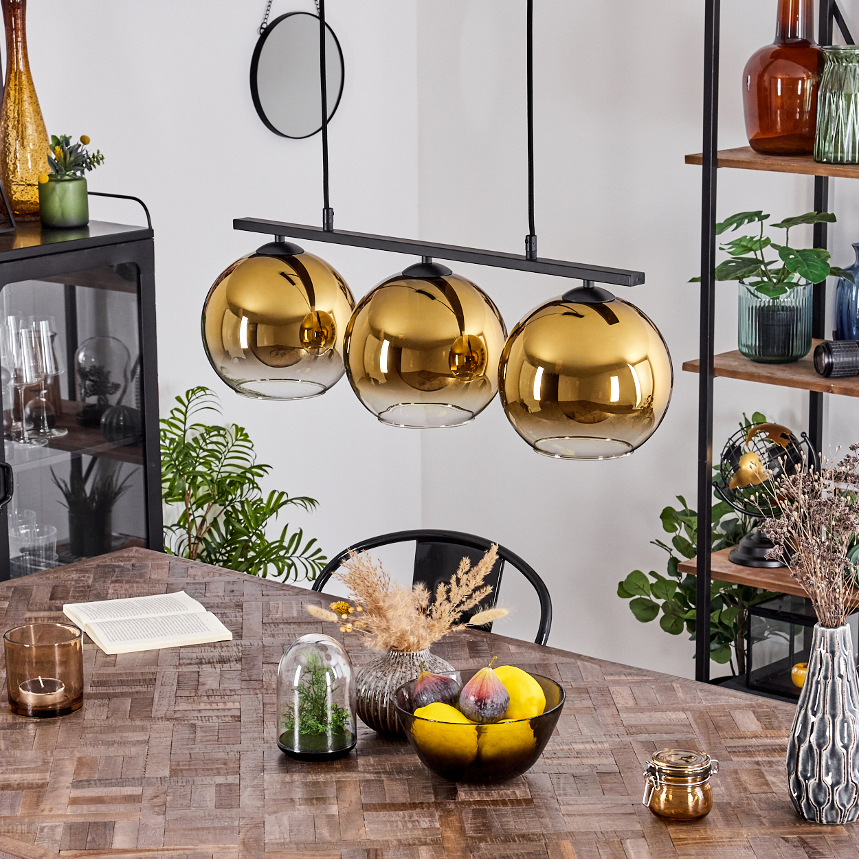 Ein Esstisch mit drei goldenen Pendelleuchten, Obstschale und Deko.