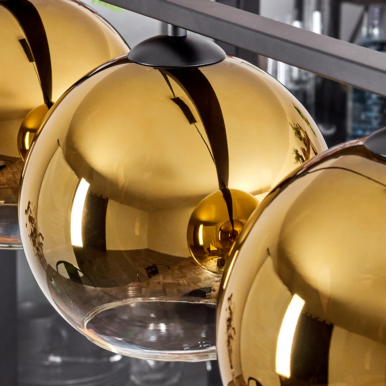 Drei goldene Kugelleuchten hängen an einer schwarzen Stange. Reflexionen sind sichtbar.