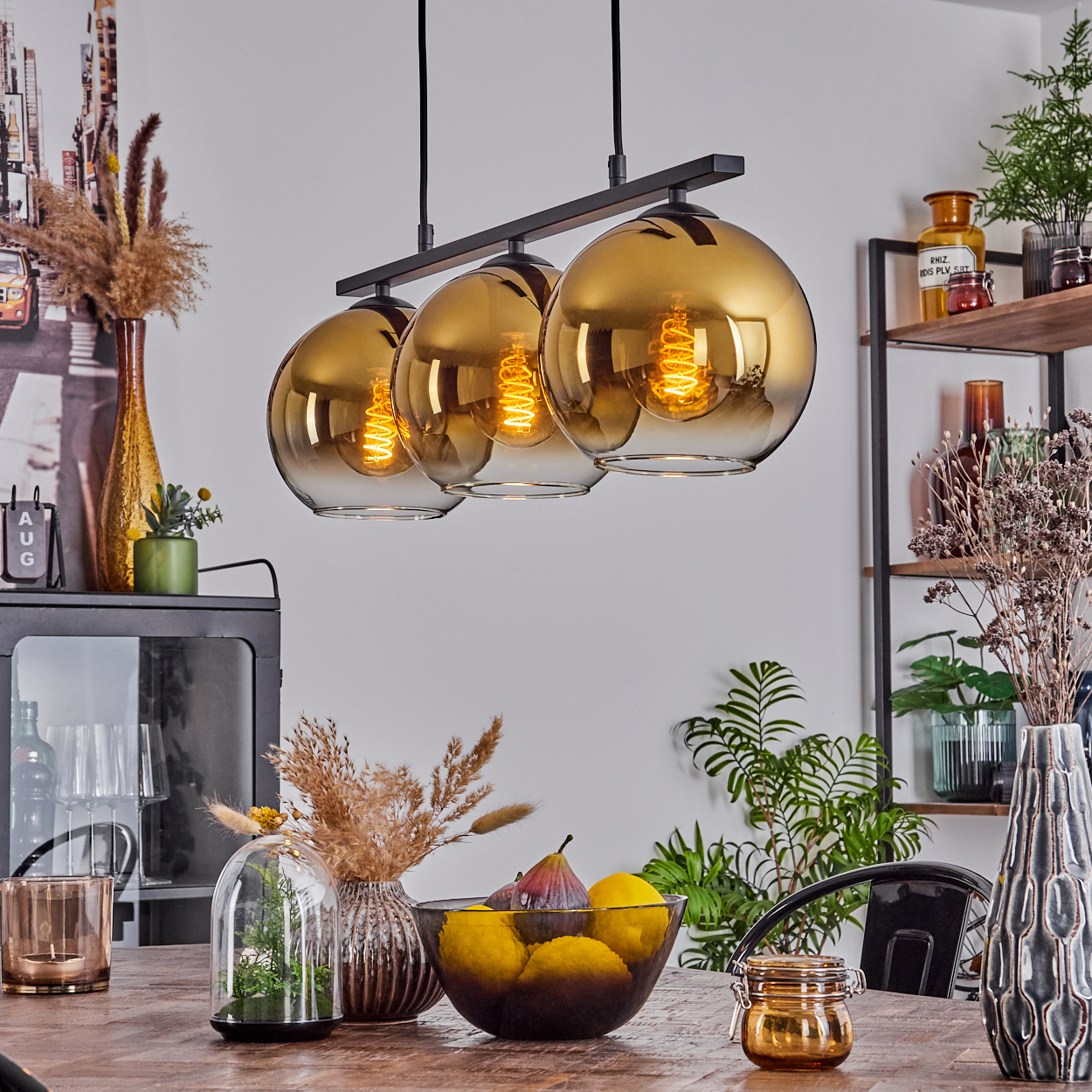 Hängeleuchte mit bernsteinfarbenen Glaskugeln über einem Holztisch mit Obst und Dekoration.