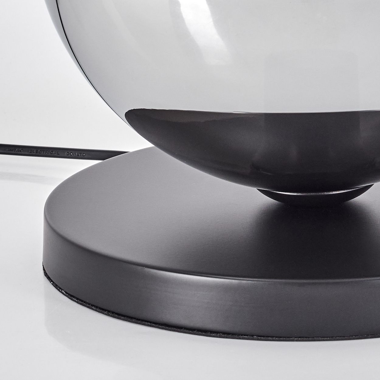 Schwarzer Sockel mit spiegelndem, dunklem Lampenschirm und Kabel.