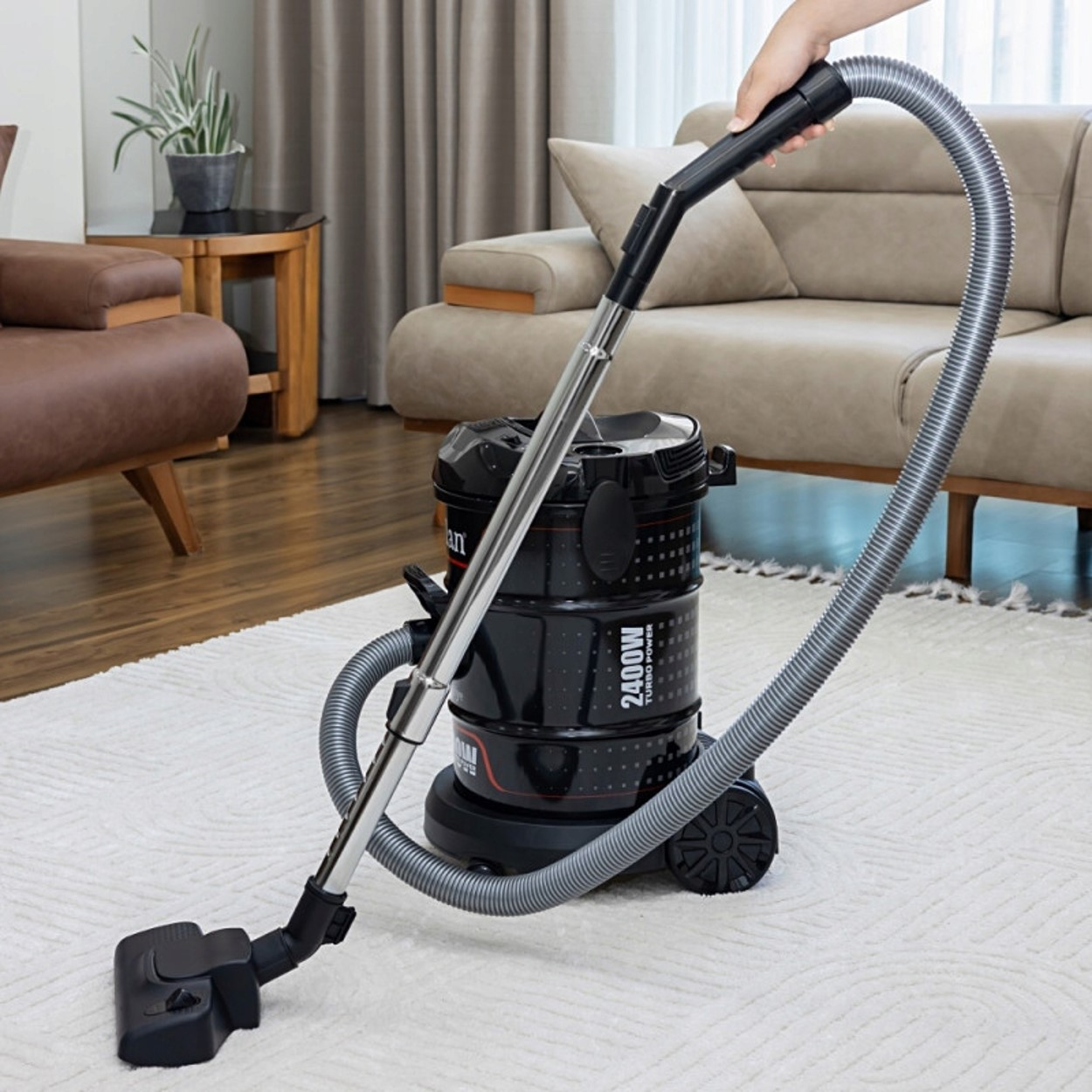 Czarny odkurzacz na białym dywanie, trzymany przez rękę, w salonie.