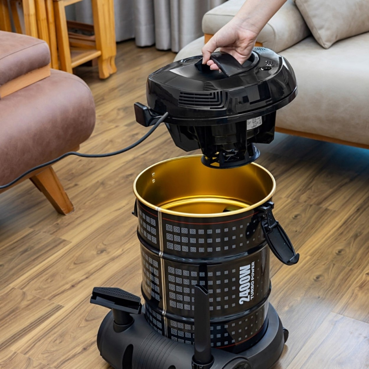 Osoba podnosi czarną głowicę odkurzacza z czarnego pojemnika ze złotym wnętrzem.