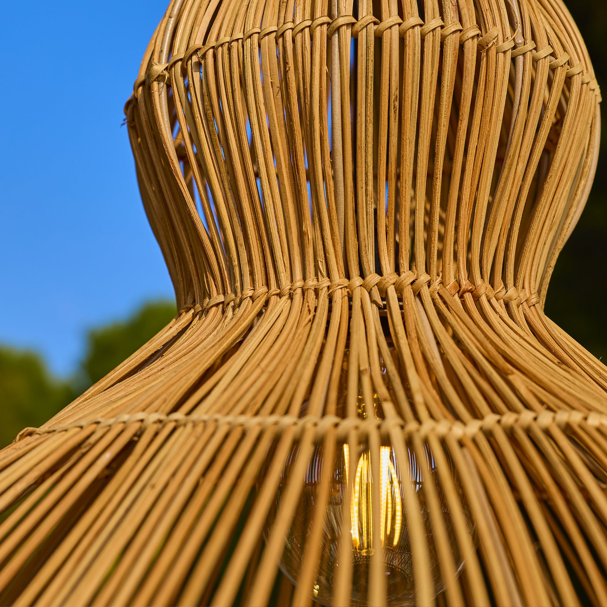 Nahaufnahme einer geflochtenen Lampe aus Naturmaterialien mit Glühbirne und blauem Himmel.