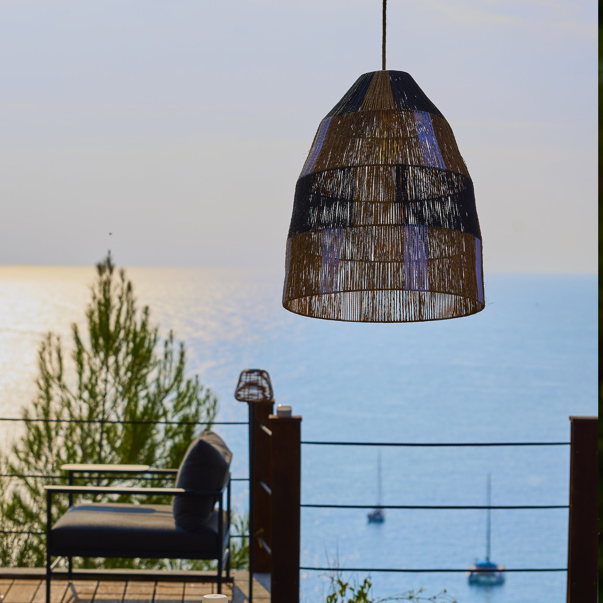 Ein Rattankorb-Hängelampenschirm über einem Meerblick-Balkon mit Sitzgelegenheiten.