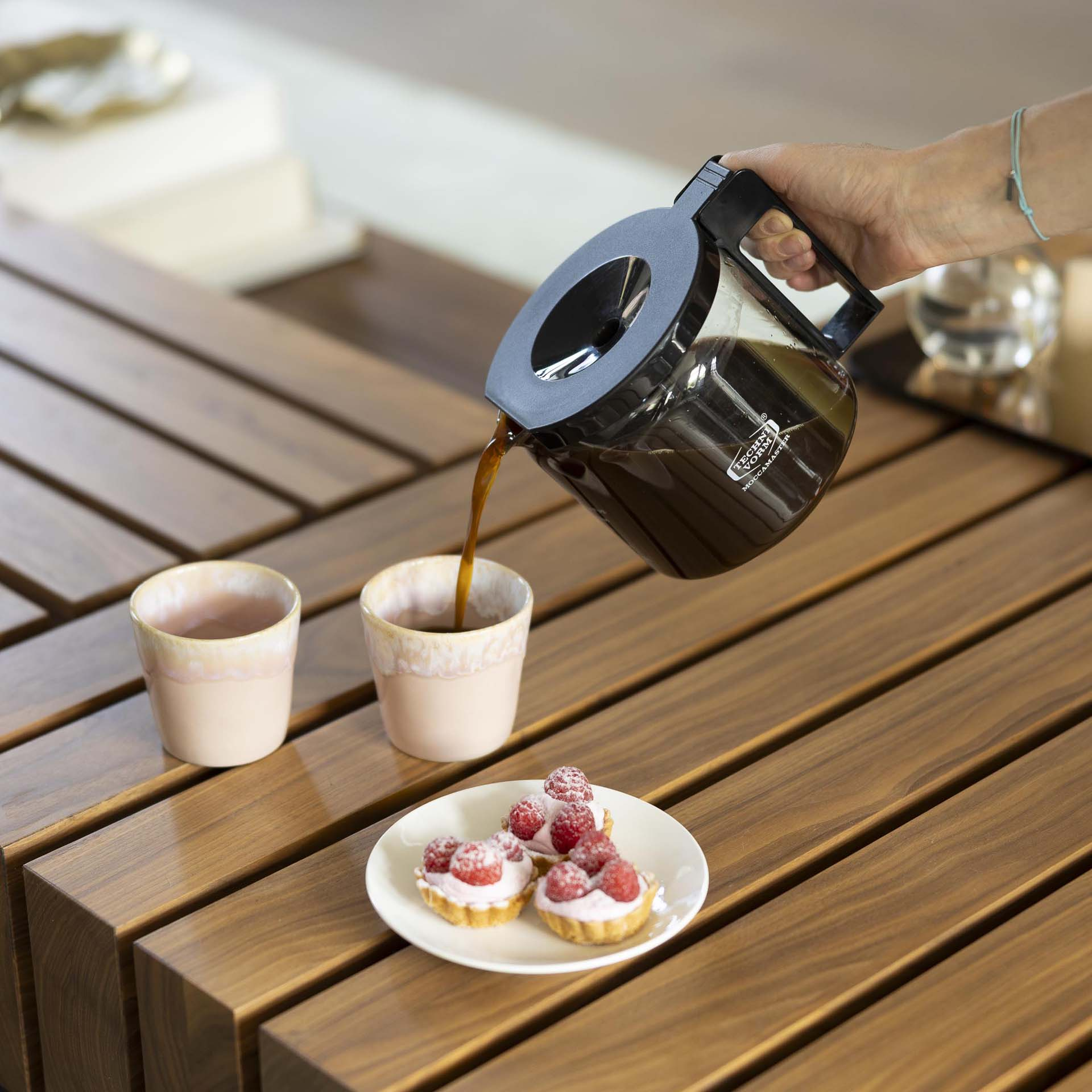 Du café est versé dans une tasse, à côté se trouvent des tartes et une autre tasse.