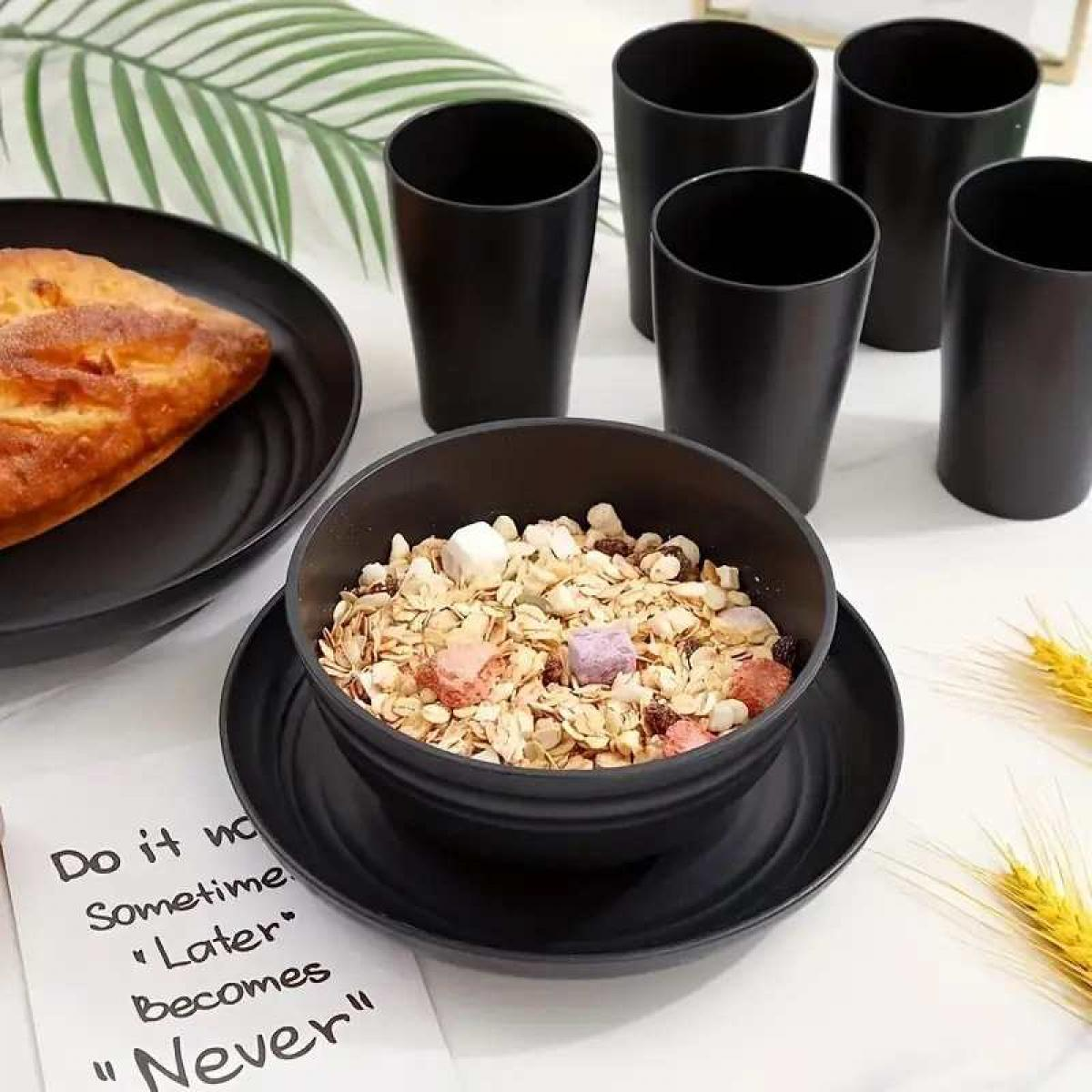 Schwarze Schüssel mit Müsli, Brot auf Teller, Tassen und Pflanzen auf weißem Hintergrund.