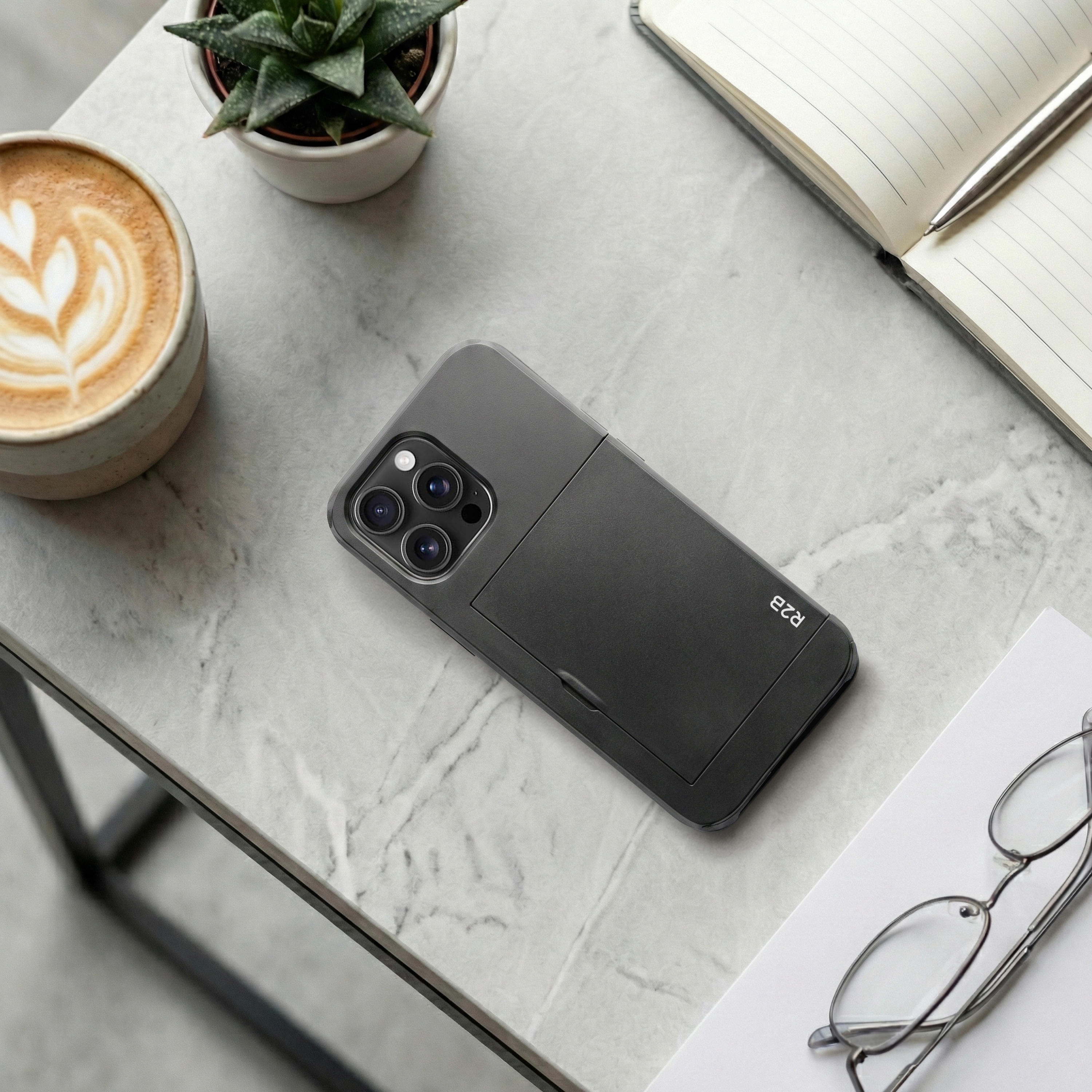 Een donkere telefoon met cameraphone ligt op een marmeren tafel naast koffie en notitieboek.