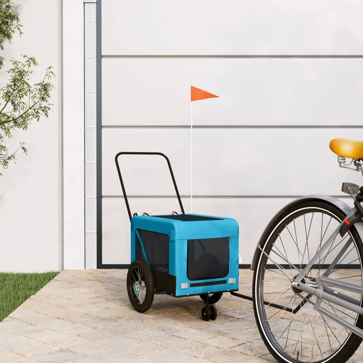 Ein blauer Fahrradanhänger mit orangem Fähnchen steht neben einem Fahrrad.