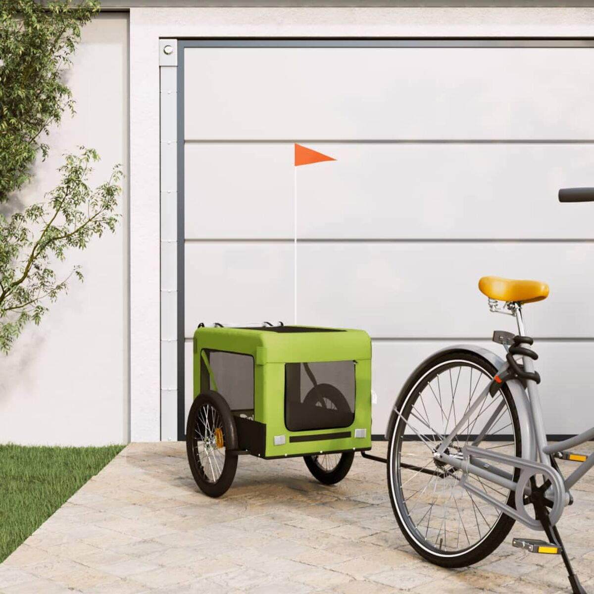 Ein grüner Fahrradanhänger mit orangefarbener Flagge steht neben einem Fahrrad vor einem Garagentor.
