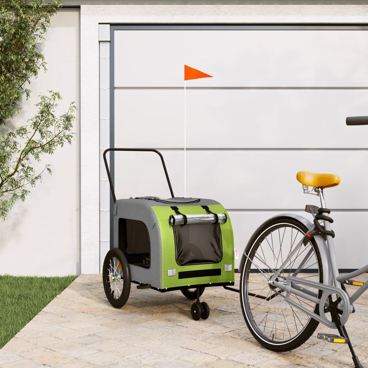 Ein grauer Fahrradanhänger mit grünen Akzenten steht neben einem Fahrrad vor einer Garage.