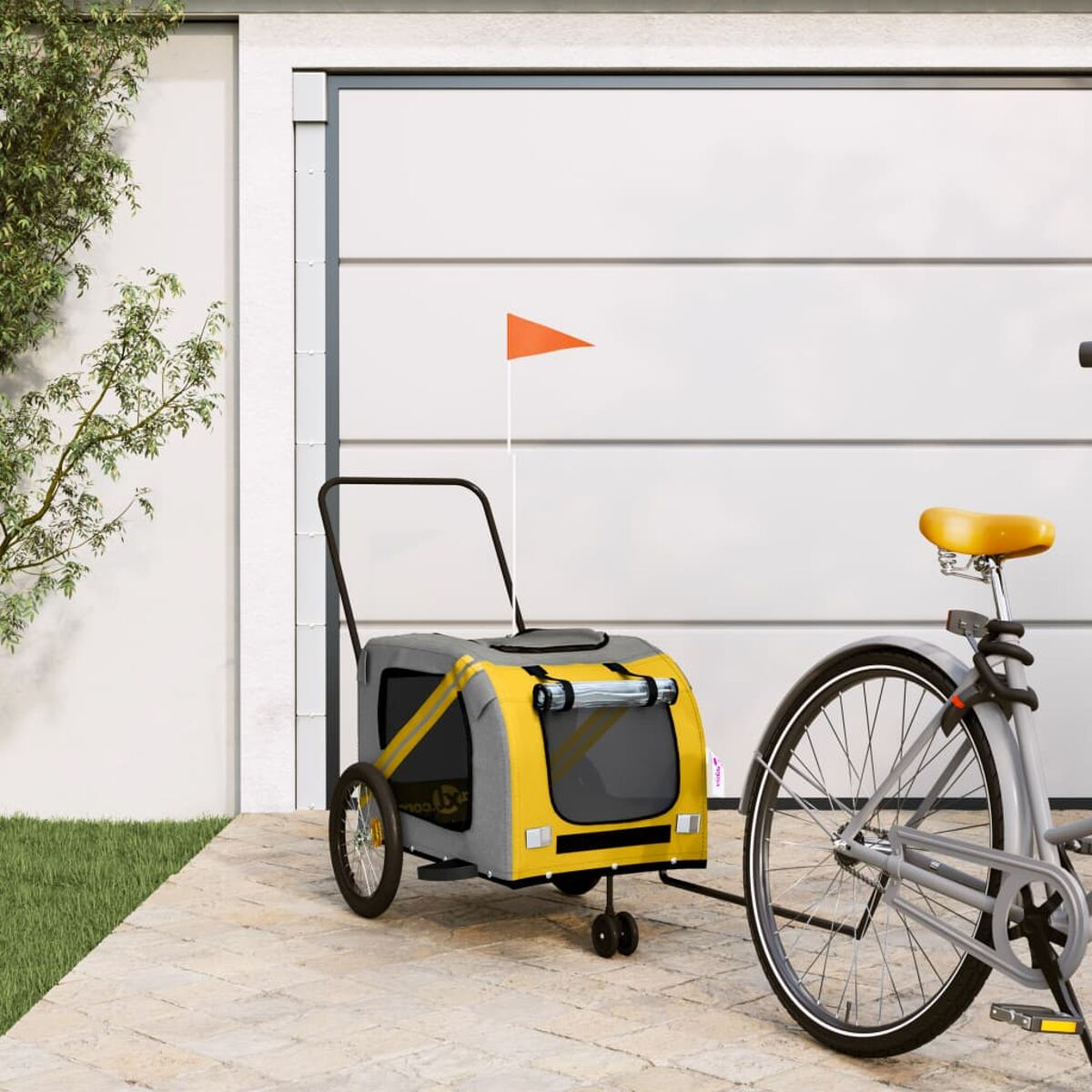 Ein gelber und grauer Hundeanhänger mit orangefarbener Fahne neben einem Fahrrad.