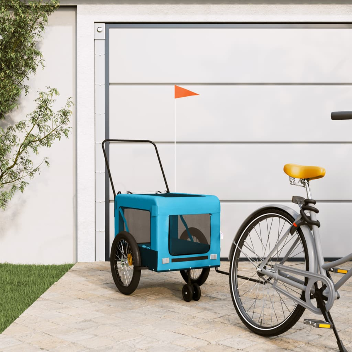Ein blauer Fahrradanhänger mit oranger Flagge steht neben einem Fahrrad vor einem Garagentor.
