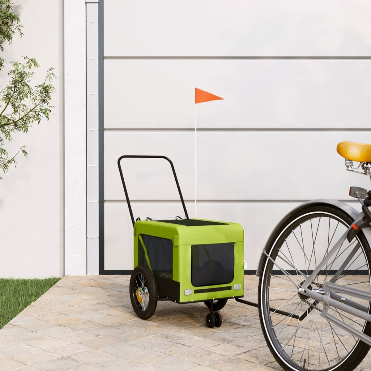 Grüner Fahrradanhänger mit orangem Fähnchen neben einem Fahrrad.