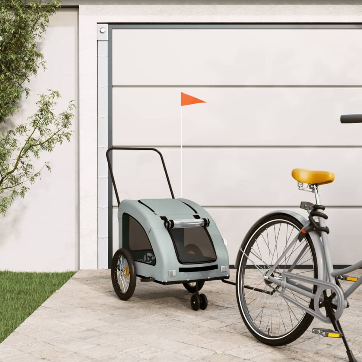 Ein grauer Fahrradanhänger mit orangefarbener Flagge steht neben einem Fahrrad vor einem Garagentor.