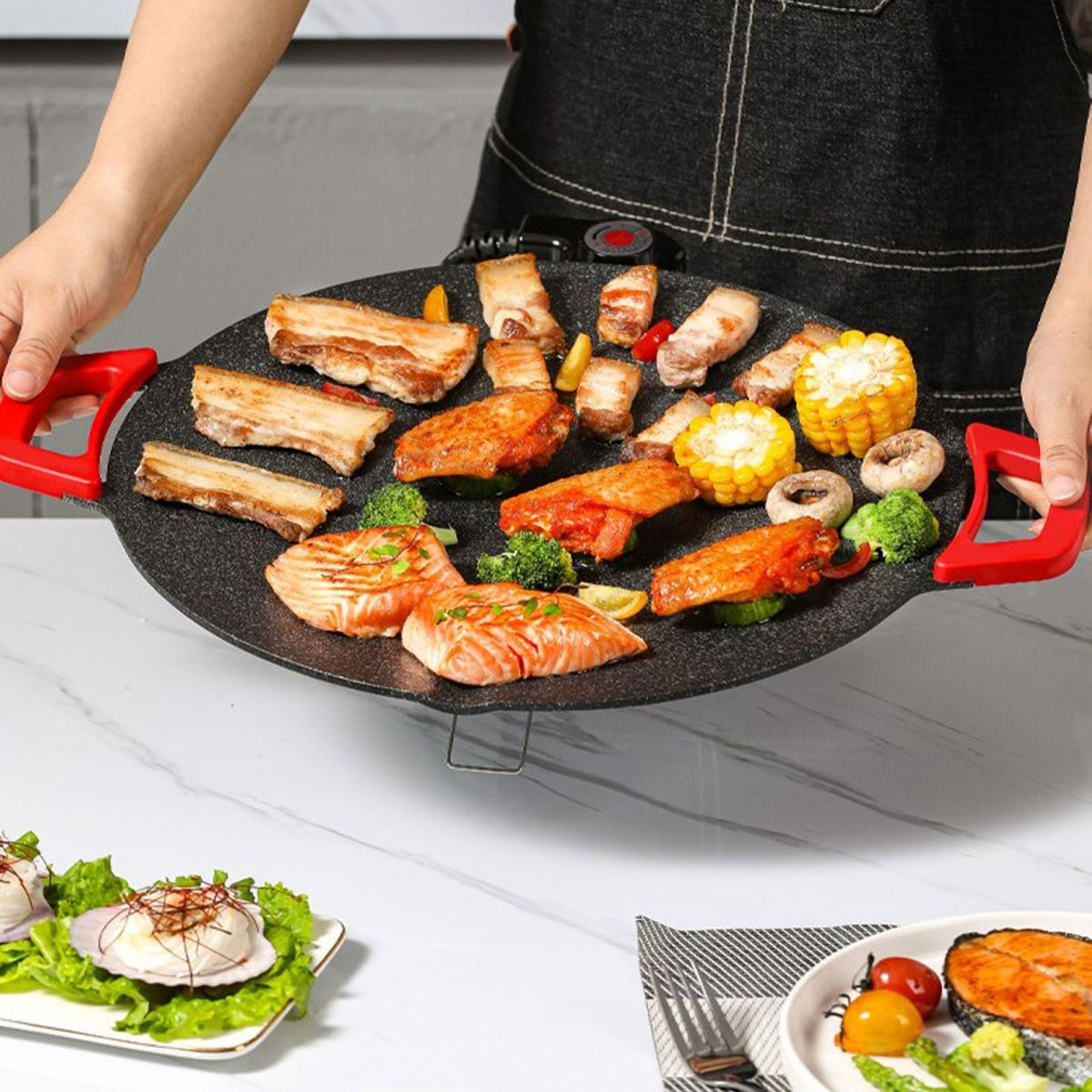Eine runde Grillplatte mit Schweinebauch, Hähnchenflügeln, Lachs, Mais, Pilzen und Brokkoli.