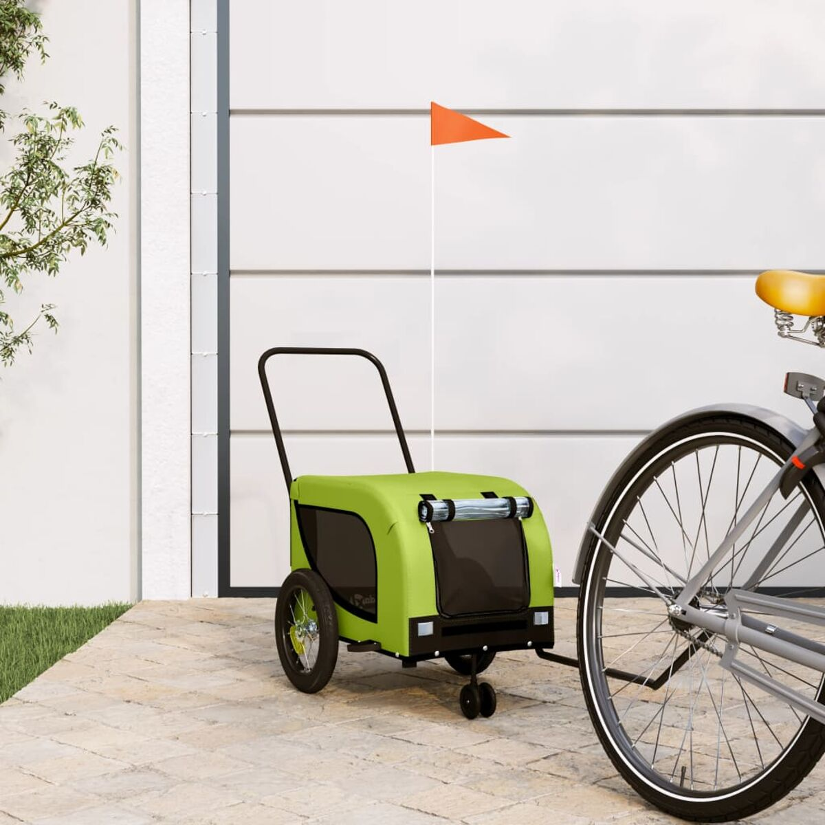 Ein grüner Fahrradanhänger mit orangener Fahne steht neben einem Fahrrad.