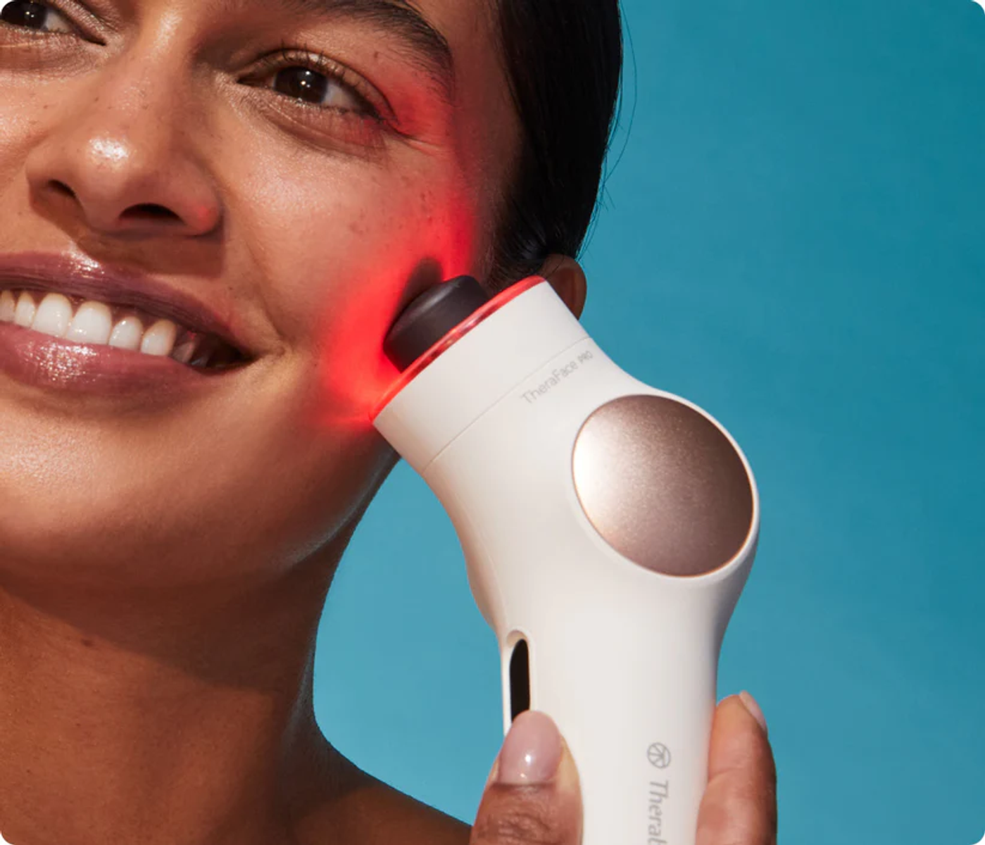 Una mujer sonríe mientras un dispositivo de cuidado de la piel con luz roja toca su cara.