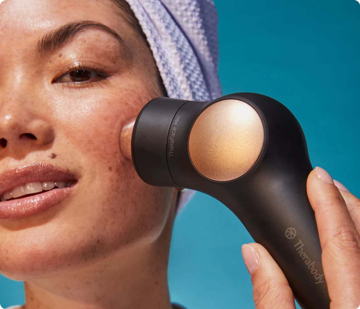 Mujer con dispositivo de tratamiento facial en la barbilla, fondo azul.