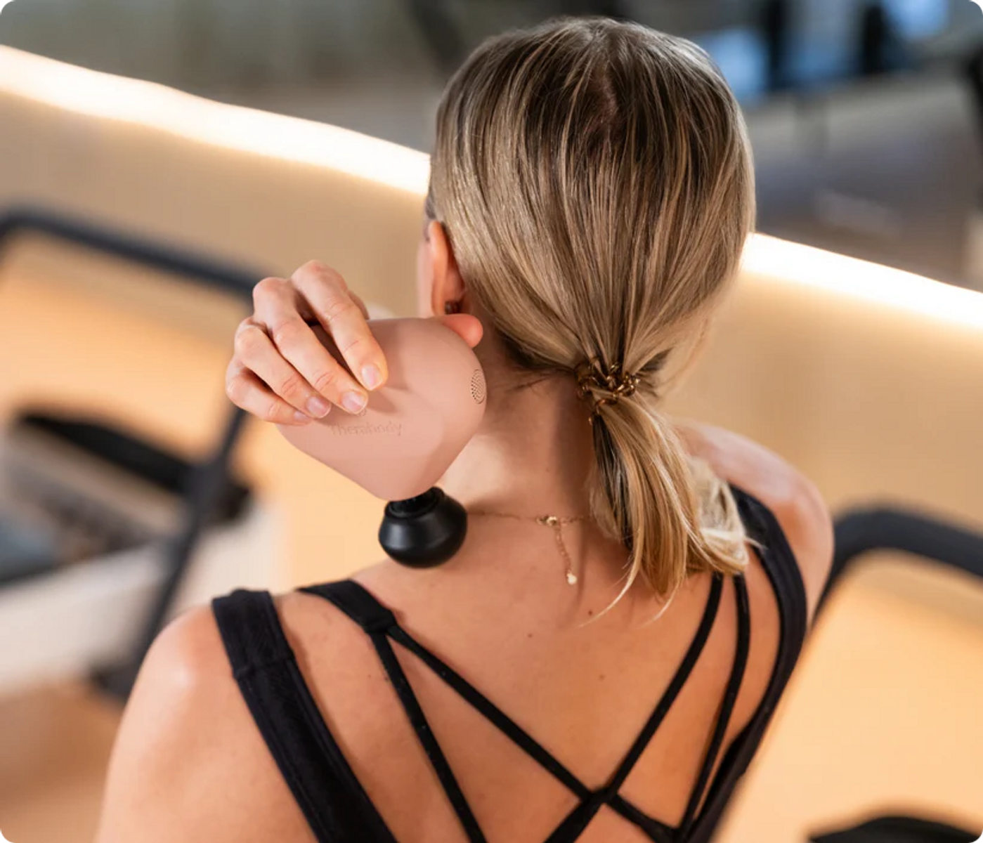 Mujer con coleta rubia usa pistola de masaje en el cuello.